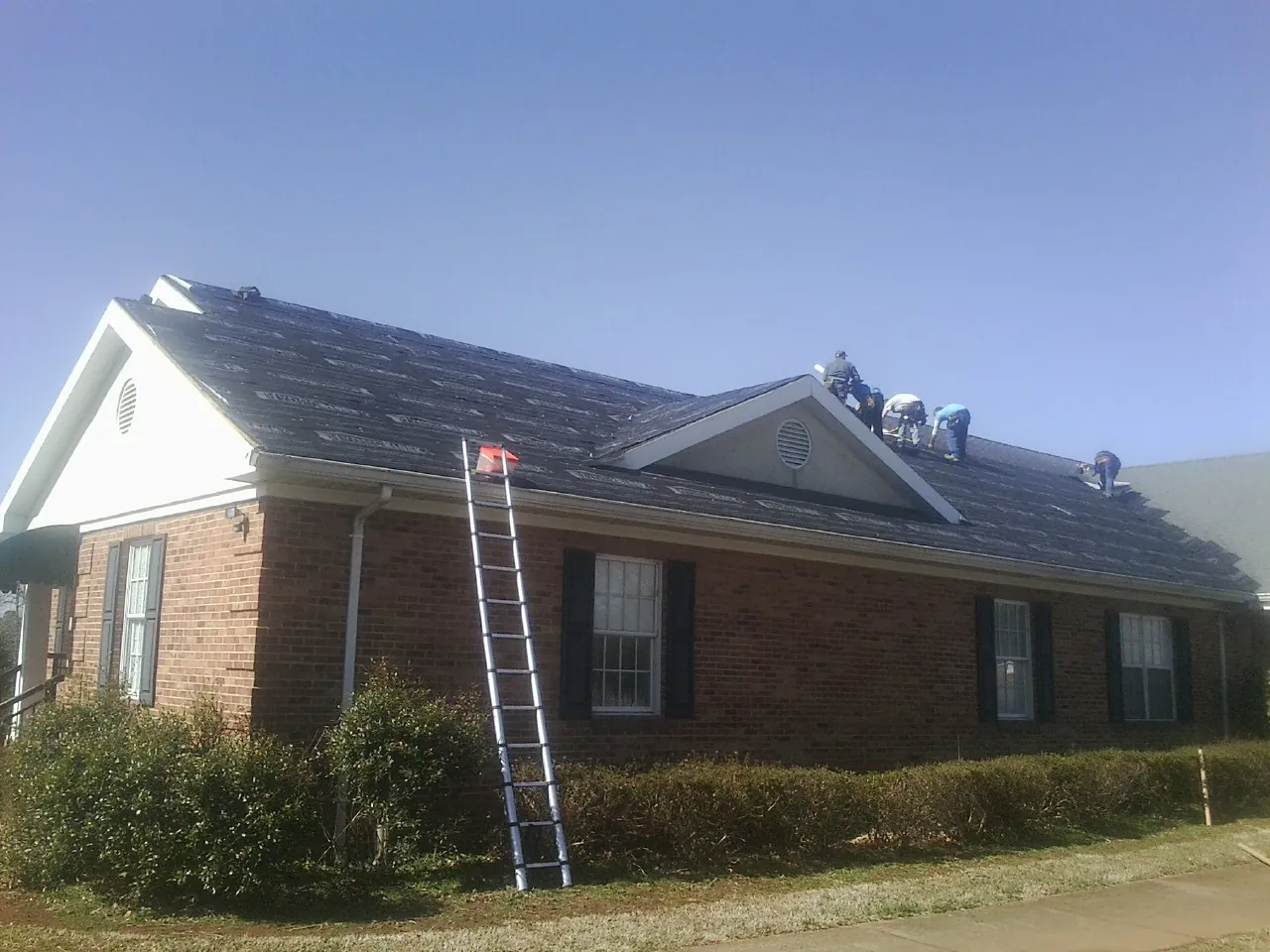 Crew tearing shingles off a brick ranch roof with a ladder set — Metal Roof Repair work by our crew in Elkhart